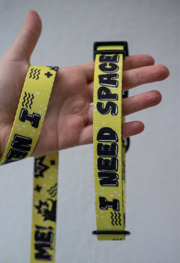 Yellow 'I Need Space' dog collar held up to show its black lettering